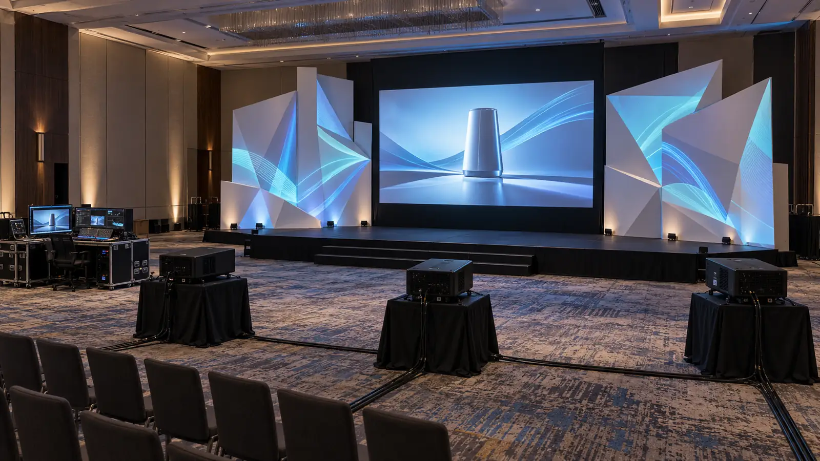 a real-world projection setup with projectors, mapped stage surfaces, a presentation screen and a control station.